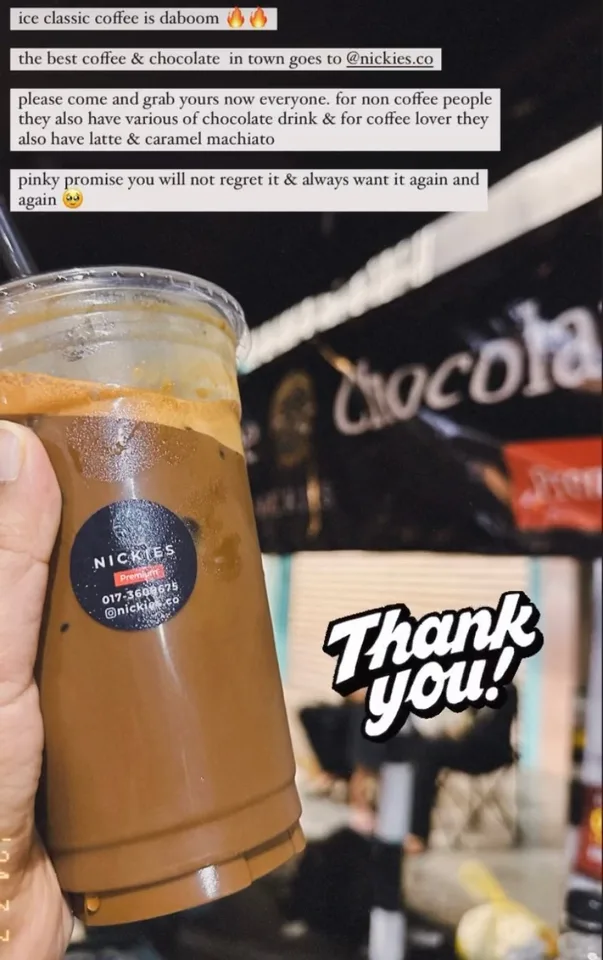 Hand holding a Nickies iced coffee in front of the Nickies stall