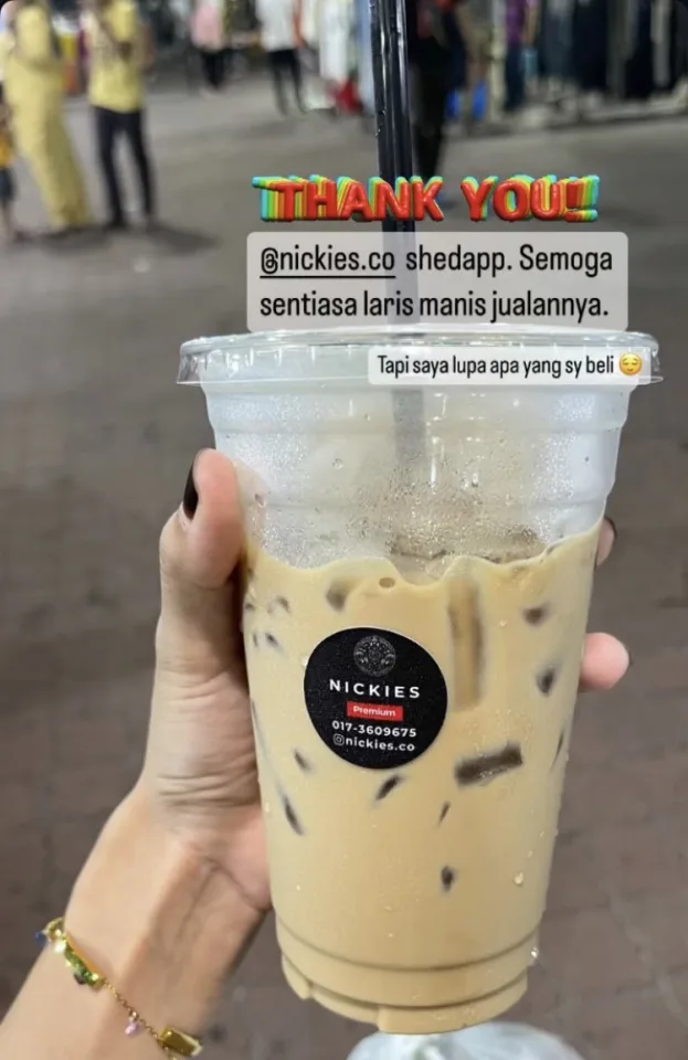Customer holding a Nickies Premium iced coffee at the night market, wishing the stall continued success